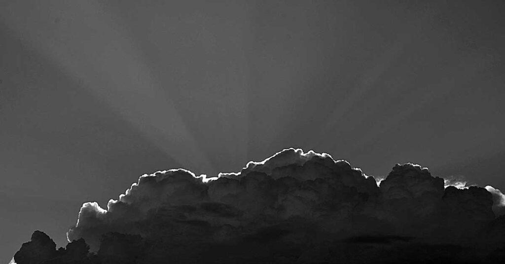 Black and white photo of a cloud with sun rays shining through, capturing a dramatic sky. Photo by Michal Jarmoluk from Pixabay.