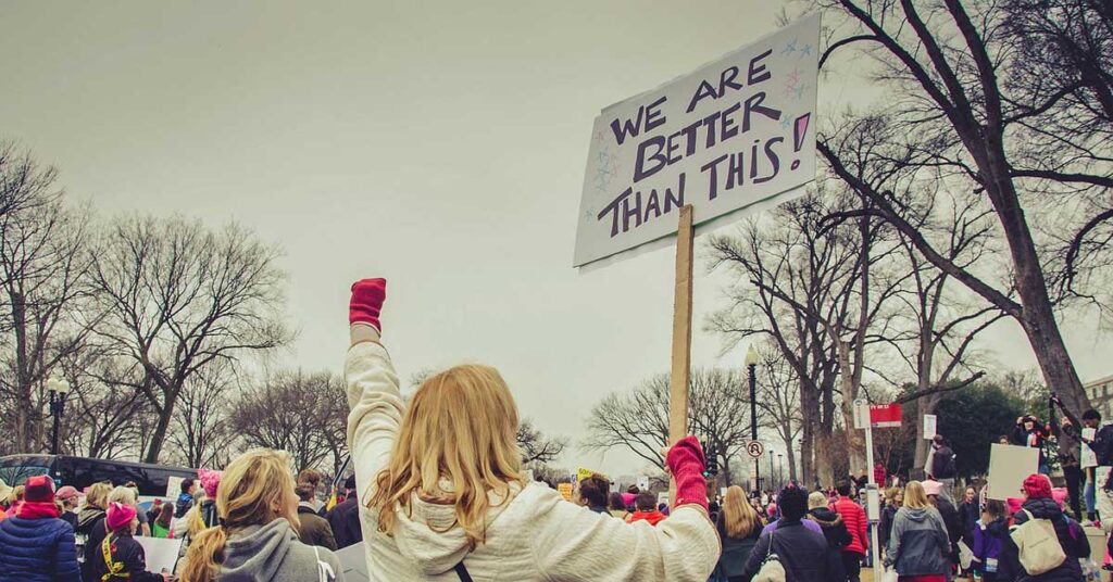 A woman displays a sign stating "We are better than this," emphasizing the need for improvement in economic and political power.
