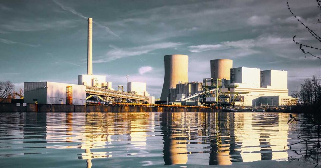 A vast power plant with water and trees nearby, representing the shift towards renewable energy sources. Photo: Peter H from Pixabay